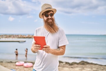 Sticker - Young redhead tourist man smiling happy using touchpad at the beach.