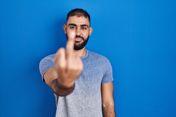 Canvas Print - Middle east man with beard standing over blue background showing middle finger, impolite and rude fuck off expression