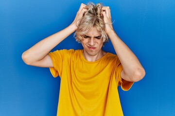 Sticker - Young modern man standing over blue background suffering from headache desperate and stressed because pain and migraine. hands on head.