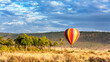 Low flying hot-air balloon in the Masai Mara, Kenya. A popular tourist excursion, shown here above the grasslands in early morning light