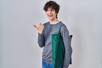 Canvas Print - Young man wearing reusable bag pointing thumb up to the side smiling happy with open mouth