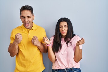 Poster - Young couple standing over isolated background excited for success with arms raised and eyes closed celebrating victory smiling. winner concept.