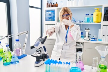 Wall Mural - Middle age blonde woman working at scientist laboratory laughing at you, pointing finger to the camera with hand over mouth, shame expression