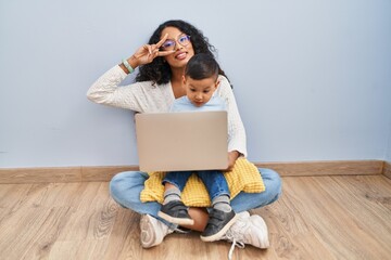 Poster - Young hispanic mother and kid using computer laptop sitting on the floor doing peace symbol with fingers over face, smiling cheerful showing victory