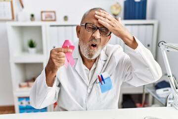 Canvas Print - Mature doctor man holding pink cancer ribbon at the clinic stressed and frustrated with hand on head, surprised and angry face