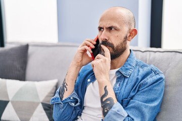 Sticker - Young bald man talking on smartphone with worried expression at home