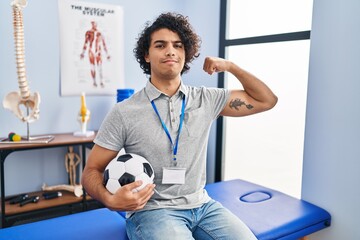 Canvas Print - Hispanic man with curly hair working as football physiotherapist strong person showing arm muscle, confident and proud of power