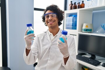 Sticker - Young hispanic man wearing scientist uniform holding bottles at laboratory