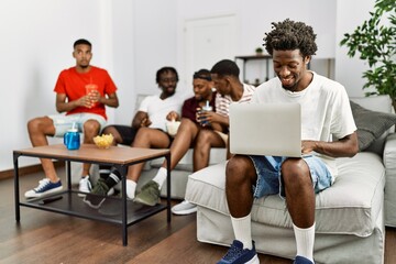 Sticker - Group of african american people sitting on the sofa at home. Man smiling happy using laptop.