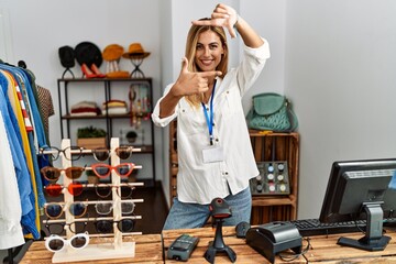 Poster - Blonde beautiful young woman working as manager at retail boutique smiling making frame with hands and fingers with happy face. creativity and photography concept.