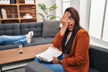 Poster - Young hispanic woman working as psychology counselor covering one eye with hand, confident smile on face and surprise emotion.