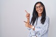 © Krakenimages.com - Young hispanic woman wearing glasses smiling and looking at the camera pointing with two hands and fingers to the side.