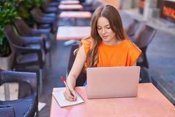 Wall Mural - Young woman using laptop writing on notebook at coffee shop terrace