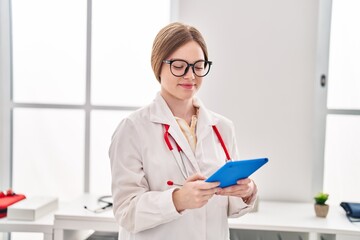 Wall Mural - Young blonde woman wearing doctor uniform using touchpad at clinic