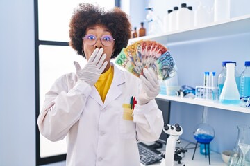 Poster - Young african american woman working at scientist laboratory holding money covering mouth with hand, shocked and afraid for mistake. surprised expression