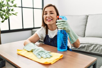 Wall Mural - Middle age hispanic woman working as housekeeper cleaning table at home