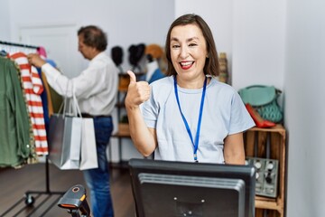 Wall Mural - Middle age hispanic woman working as manager at retail boutique smiling happy and positive, thumb up doing excellent and approval sign