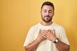 © Krakenimages.com - Handsome hispanic man standing over yellow background smiling with hands on chest with closed eyes and grateful gesture on face. health concept.