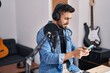 © Krakenimages.com - Young hispanic man artist smiling confident using smartphone at music studio