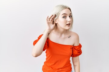 Poster - Young caucasian woman standing over isolated background smiling with hand over ear listening an hearing to rumor or gossip. deafness concept.