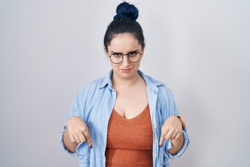 Sticker - Young modern girl with blue hair standing over white background pointing down looking sad and upset, indicating direction with fingers, unhappy and depressed.