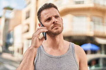 Wall Mural - Young hispanic man talking on the smartphone with serious expression at street