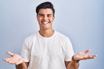 Sticker - Hispanic man standing over blue background smiling cheerful offering hands giving assistance and acceptance.