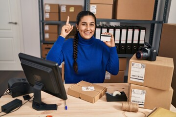 Sticker - Young hispanic woman working at small business ecommerce holding credit card surprised with an idea or question pointing finger with happy face, number one