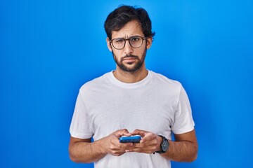 Sticker - Handsome latin man using smartphone typing message skeptic and nervous, frowning upset because of problem. negative person.