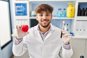 Canvas Print - Arab man with beard working at scientist laboratory holding blood samples smiling with a happy and cool smile on face. showing teeth.