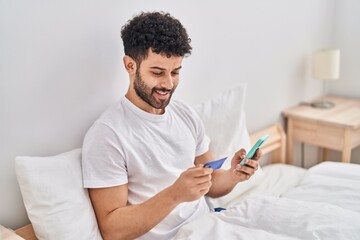 Sticker - Young arab man using smartphone and credit card sitting on bed at bedroom