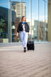 © mimagephotos - Full length happy travel woman walking in city with suitcase