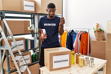 Canvas Print - Young african american volunteer man packing donations box for charity doing money gesture with hands, asking for salary payment, millionaire business