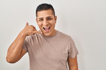 Poster - Hispanic young man standing over white background smiling doing phone gesture with hand and fingers like talking on the telephone. communicating concepts.