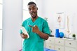 © Krakenimages.com - Young african physiotherapist man holding massage body lotion smiling happy pointing with hand and finger