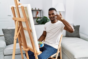 Canvas Print - Young african man painting on canvas at home pointing with hand finger to face and nose, smiling cheerful. beauty concept