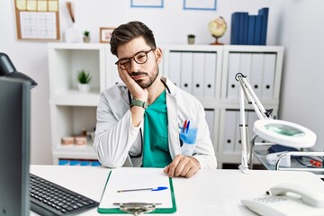  Young man with beard wearing doctor uniform and stethoscope at the clinic thinking looking tired and bored with depression problems with crossed arms.