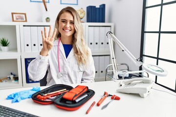 Poster - Young beautiful doctor woman with reflex hammer and medical instruments showing and pointing up with fingers number four while smiling confident and happy.