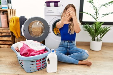 Canvas Print - Young beautiful woman doing laundry sitting by wicker basket covering eyes with hands and doing stop gesture with sad and fear expression. embarrassed and negative concept.