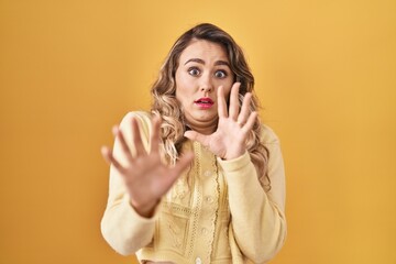 Canvas Print - Young caucasian woman standing over yellow background afraid and terrified with fear expression stop gesture with hands, shouting in shock. panic concept.