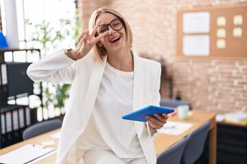 Canvas Print - Young caucasian woman working at the office wearing glasses doing peace symbol with fingers over face, smiling cheerful showing victory