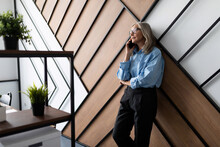 Fifty Year Old Successful Business Woman Executive Talking On Mobile Phone Leaning Against The Wall In The Office. Professional Accountant Woman Doing Accounting Finance Invoice Concept