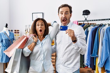 Poster - Hispanic middle age couple holding shopping bags and credit card crazy and scared with hands on head, afraid and surprised of shock with open mouth