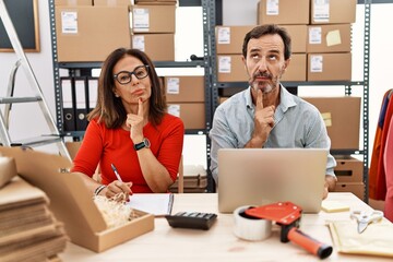 Wall Mural - Middle age couple working at small business ecommerce thinking concentrated about doubt with finger on chin and looking up wondering