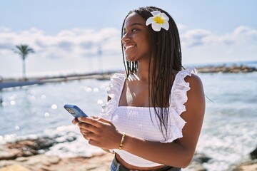 Canvas Print - Young african american girl smiling happy using smartphone at the beach