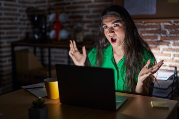 Sticker - Young teenager girl working at the office at night crazy and mad shouting and yelling with aggressive expression and arms raised. frustration concept.