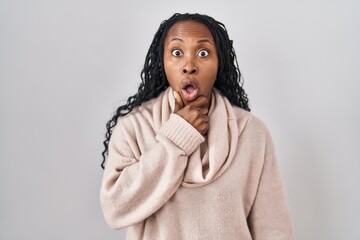 Canvas Print - African woman standing over white background looking fascinated with disbelief, surprise and amazed expression with hands on chin