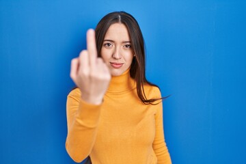 Poster - Young brunette woman standing over blue background showing middle finger, impolite and rude fuck off expression