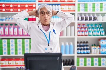 Wall Mural - Middle age woman with tattoos working at pharmacy drugstore crazy and scared with hands on head, afraid and surprised of shock with open mouth