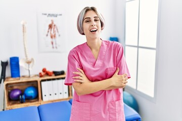 Sticker - Young nurse woman working at pain recovery clinic happy face smiling with crossed arms looking at the camera. positive person.